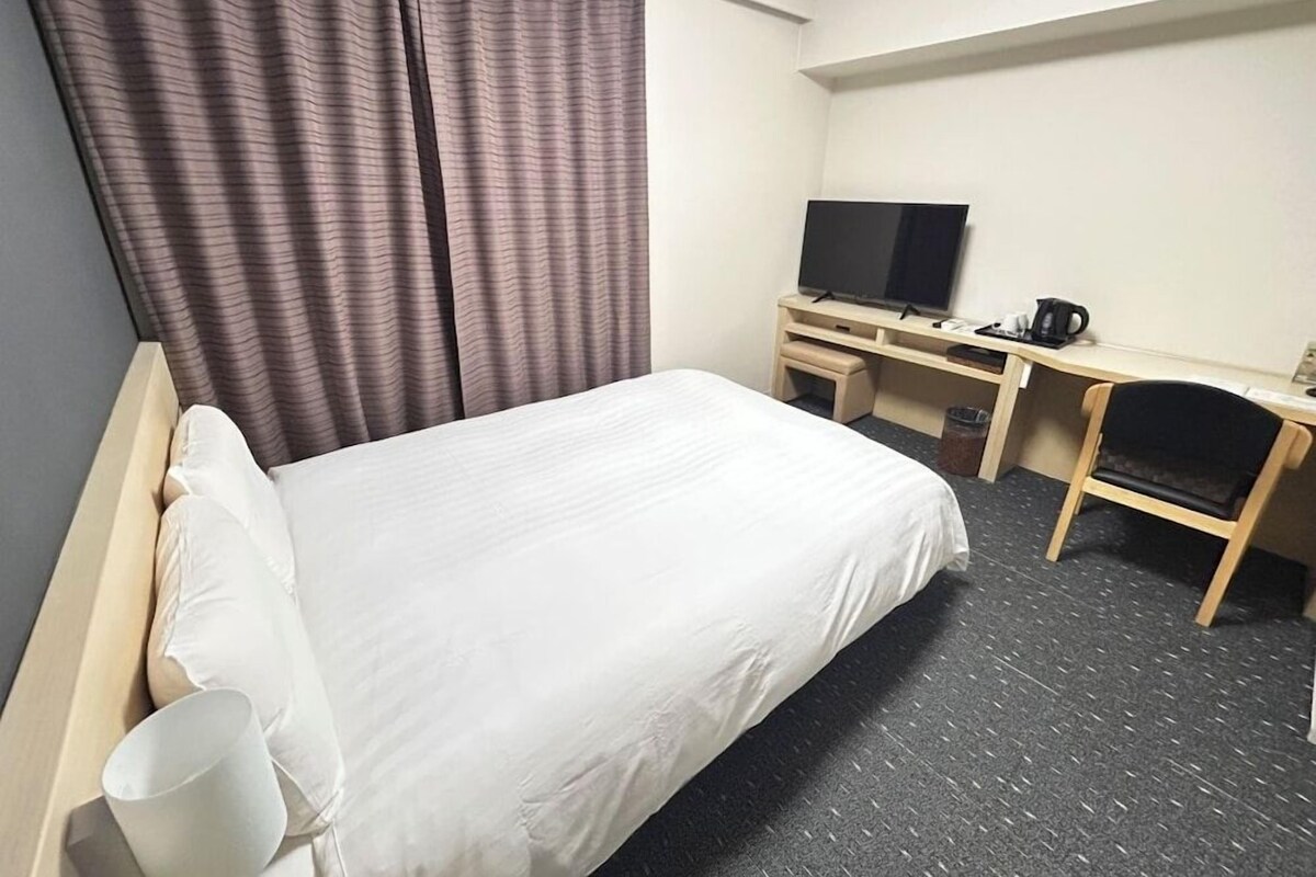 A hotel room with a bed, a desk with a television, and a chair.