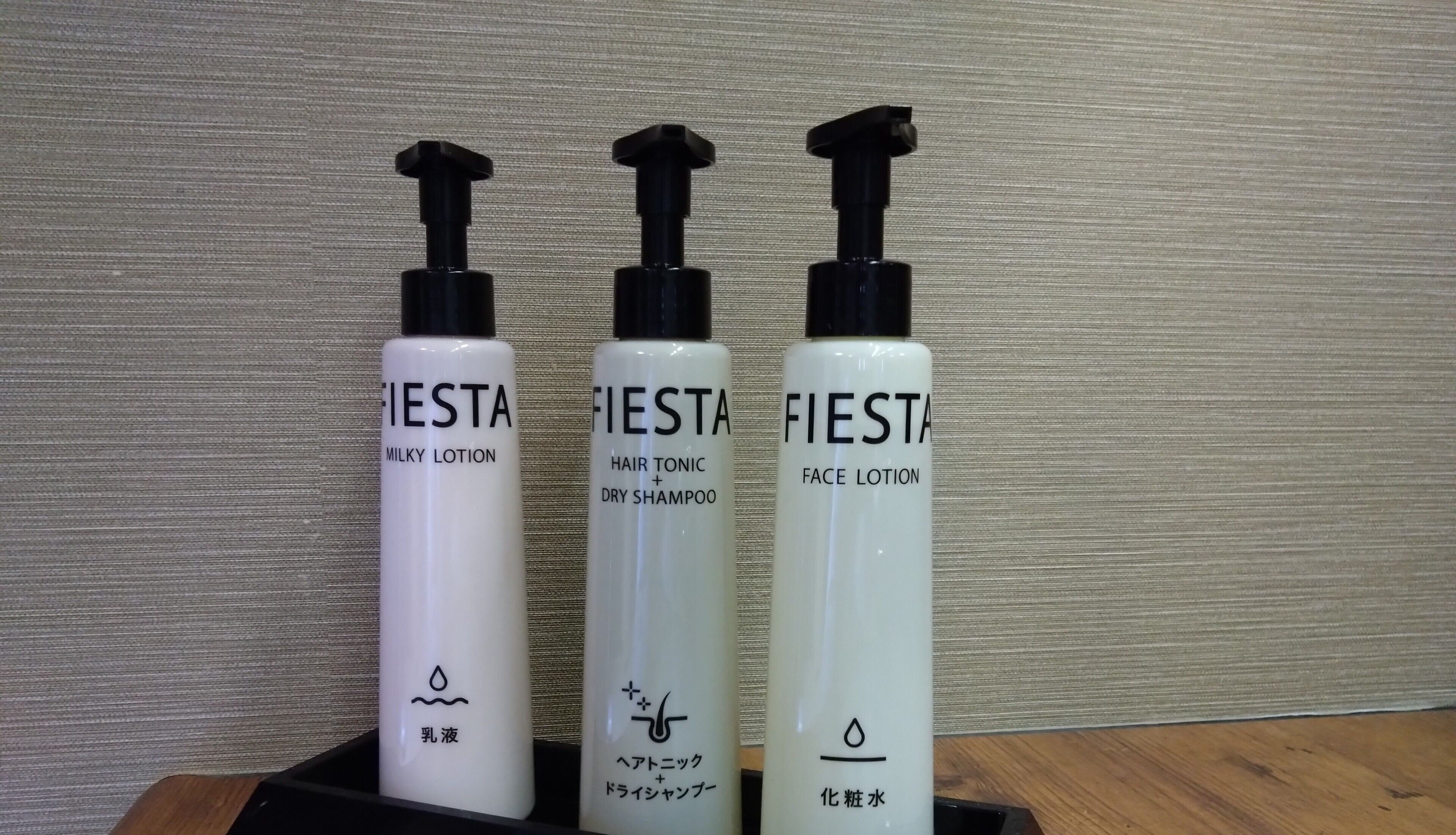 Three bottles of FIesta products in a black tray against a textured wall.
