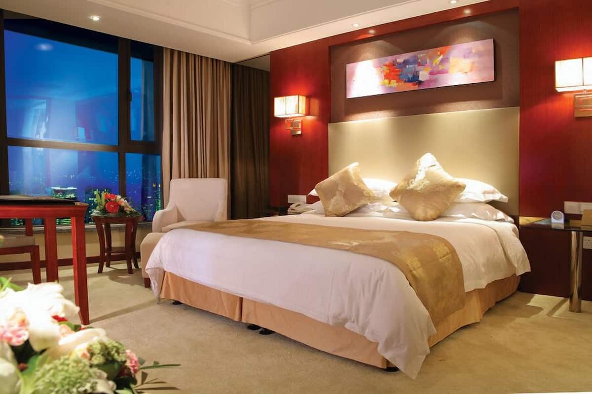 A hotel room with a large bed, a desk, and a view of the city at night.