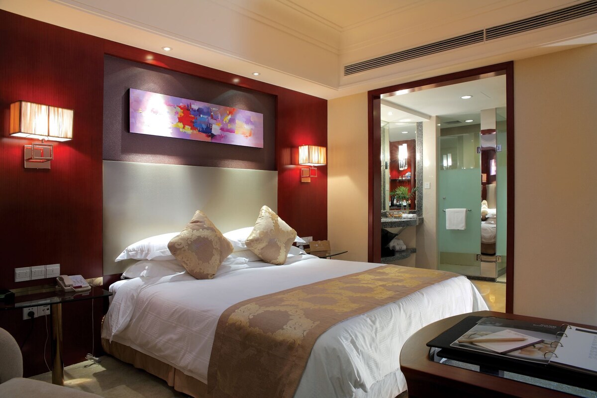 A hotel room with a large bed, a desk, and a mirror.