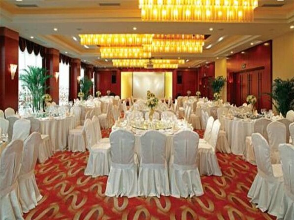 Une salle de banquet avec des tables rondes, des chaises blanches et une moquette rouge.