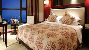 A hotel room with a large bed, a nightstand, a lamp, and a view of the city at night. - Yuloon Hotel Shanghai (Shanghai)