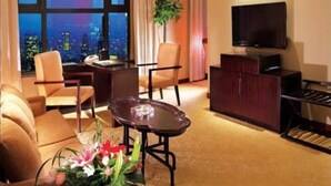 A hotel room with a large window, a flat-screen TV, a desk with a chair, a sofa, and a small table with flowers. - Yuloon Hotel Shanghai (Shanghai)