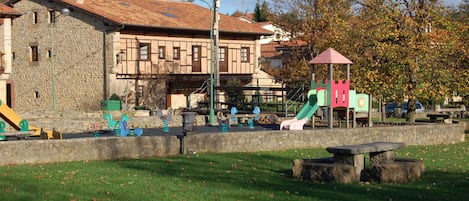 Een park met speeltoestellen, een stenen gebouw en een picknickplaats.