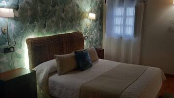 A neatly made bed with a headboard, two bedside lamps, and a window with sheer curtains.