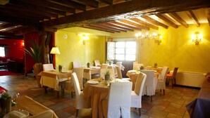 A dining area with tables set for four, wooden beams on the ceiling, and a large window with curtains. - La Casona de Revolgo (Santillana del Mar)