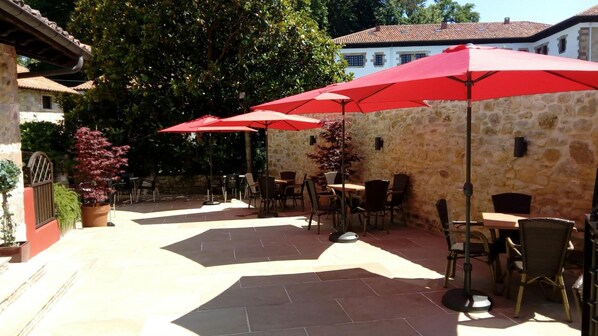 Eine Außenpatio-Terrasse mit Steinmauern, roten Sonnenschirmen und Gartenmöbeln.
