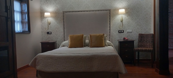 Ein Schlafzimmer mit einem großen Bett, zwei Nachttischlampen, einem Nachttisch, einem Sessel und einem Fenster mit Vorhängen.