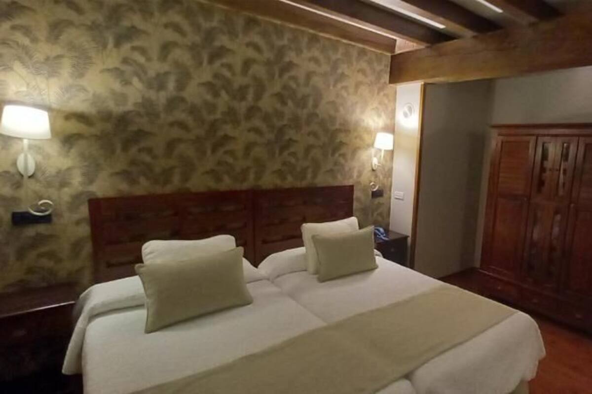 Habitació d'hotel amb un llit, dues làmpades de nit, un armari de fusta i una banca.