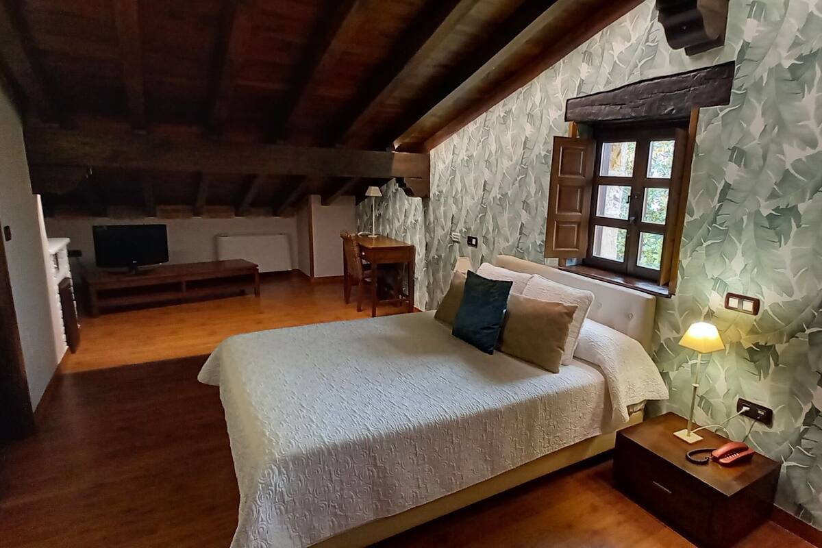 Un dormitori amb llit, taula de nit, làmpada i finestra amb cortines.