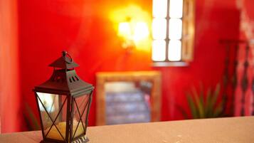 A close-up of a dark brown lantern on a beige surface with a red wall and a window in the background.