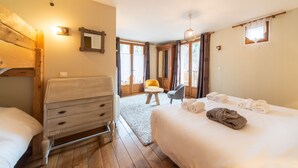 A hotel room with a wooden bed, a small desk, a chair, a window with curtains, and a view of the outdoors. - Maison Caramel (Landry)