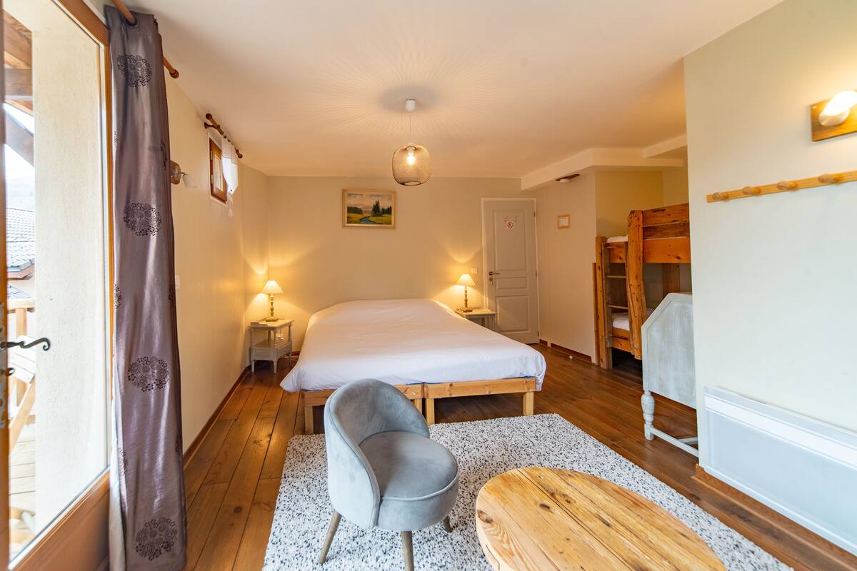 Une chambre à coucher comprenant un lit, des tables de chevet, une chaise, un banc en bois, une porte et un luminaire fixé au mur.