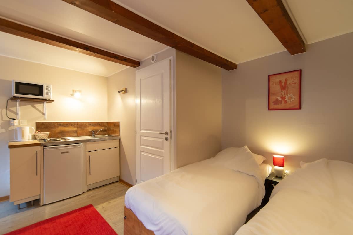 Une chambre à coucher de taille réduite, avec un lit simple, une petite kitchenette et une porte donnant sur une autre pièce.