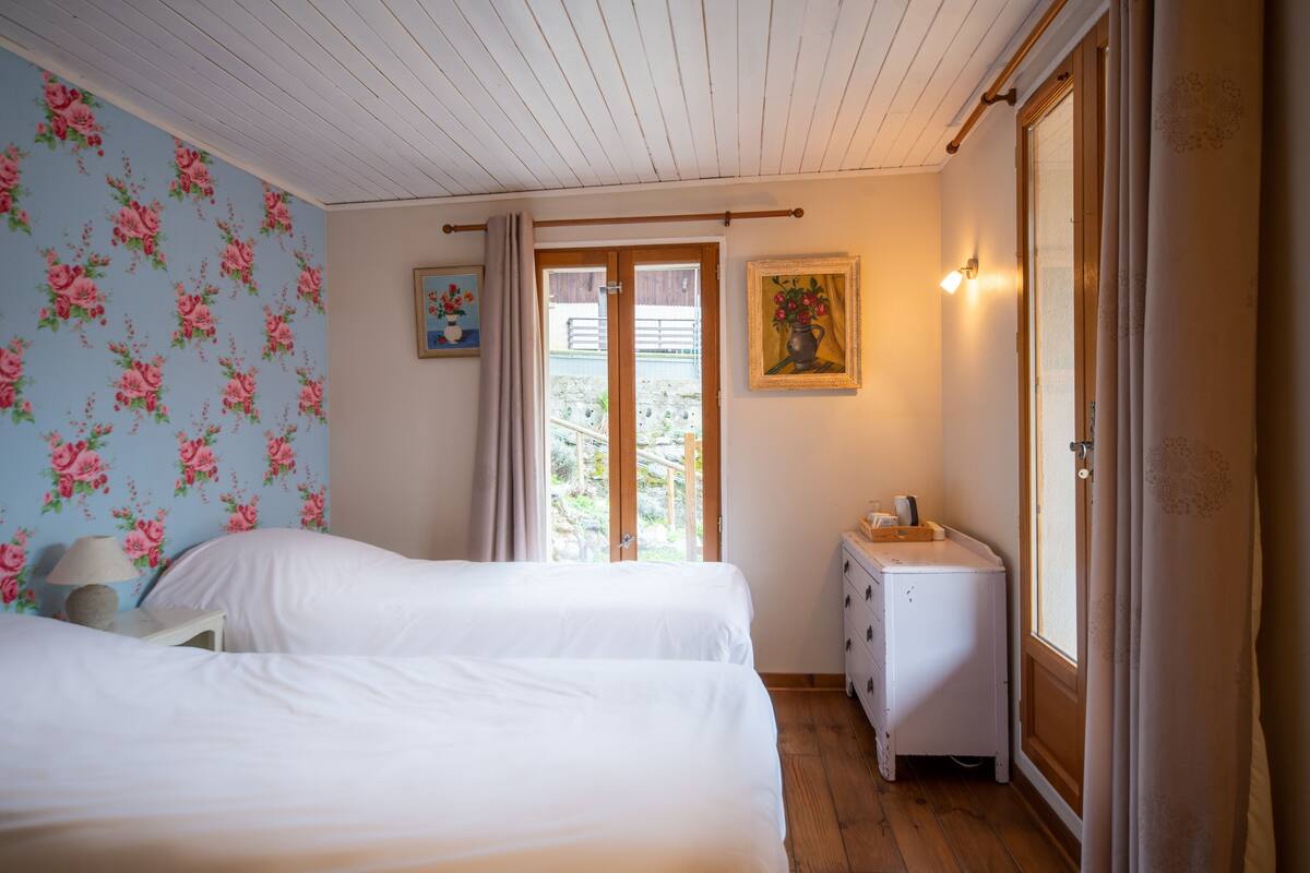 Une chambre avec deux lits, une commode, une table de chevet, une lampe et une fenêtre avec des rideaux.