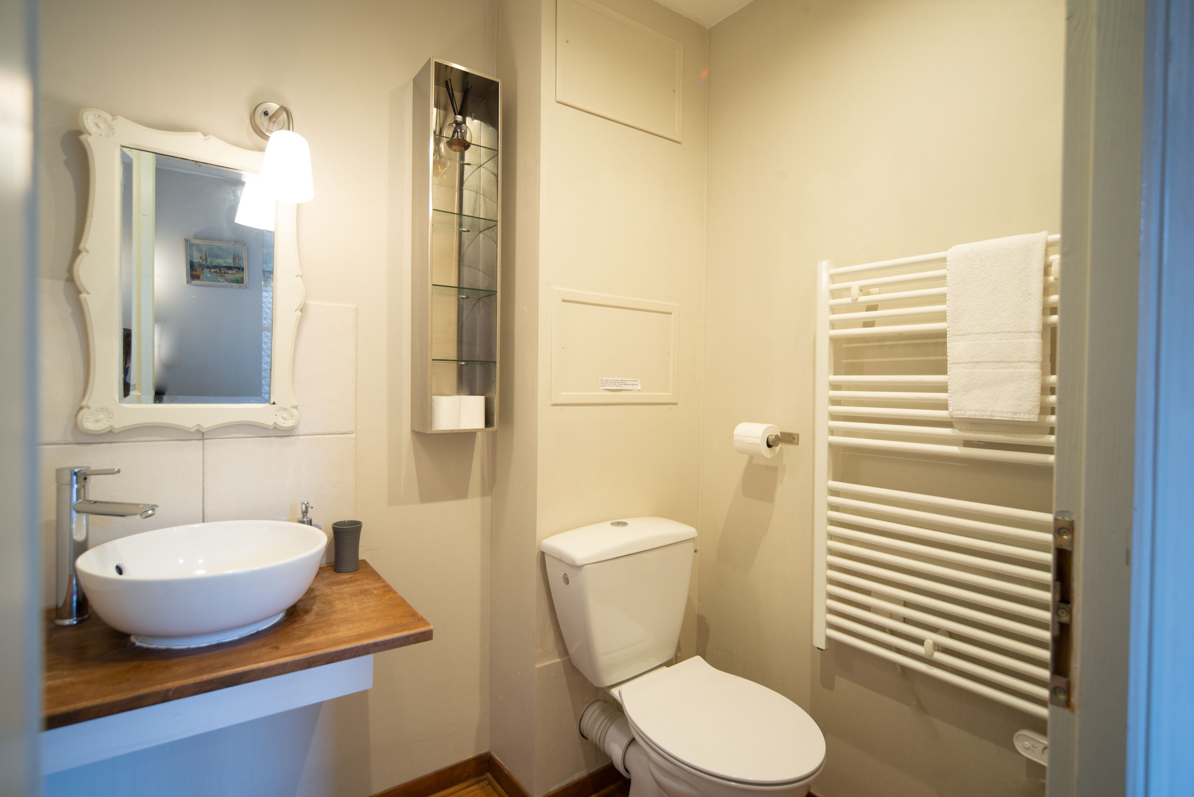 Et badeværelse med vask, toilet, spejl og håndklædestativ.
