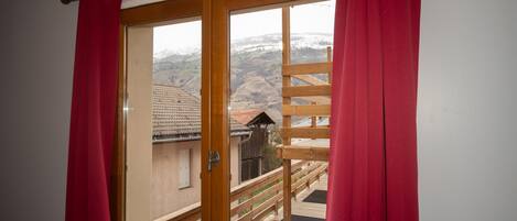 Una habitación con balcón de madera, vista a un paisaje montañoso y una cortina roja.
