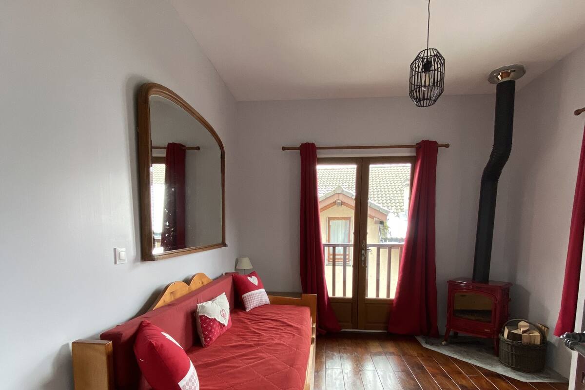 Une chambre à coucher avec un lit en bois, un miroir, un rideau rouge, un plancher en bois et un radiateur rouge.