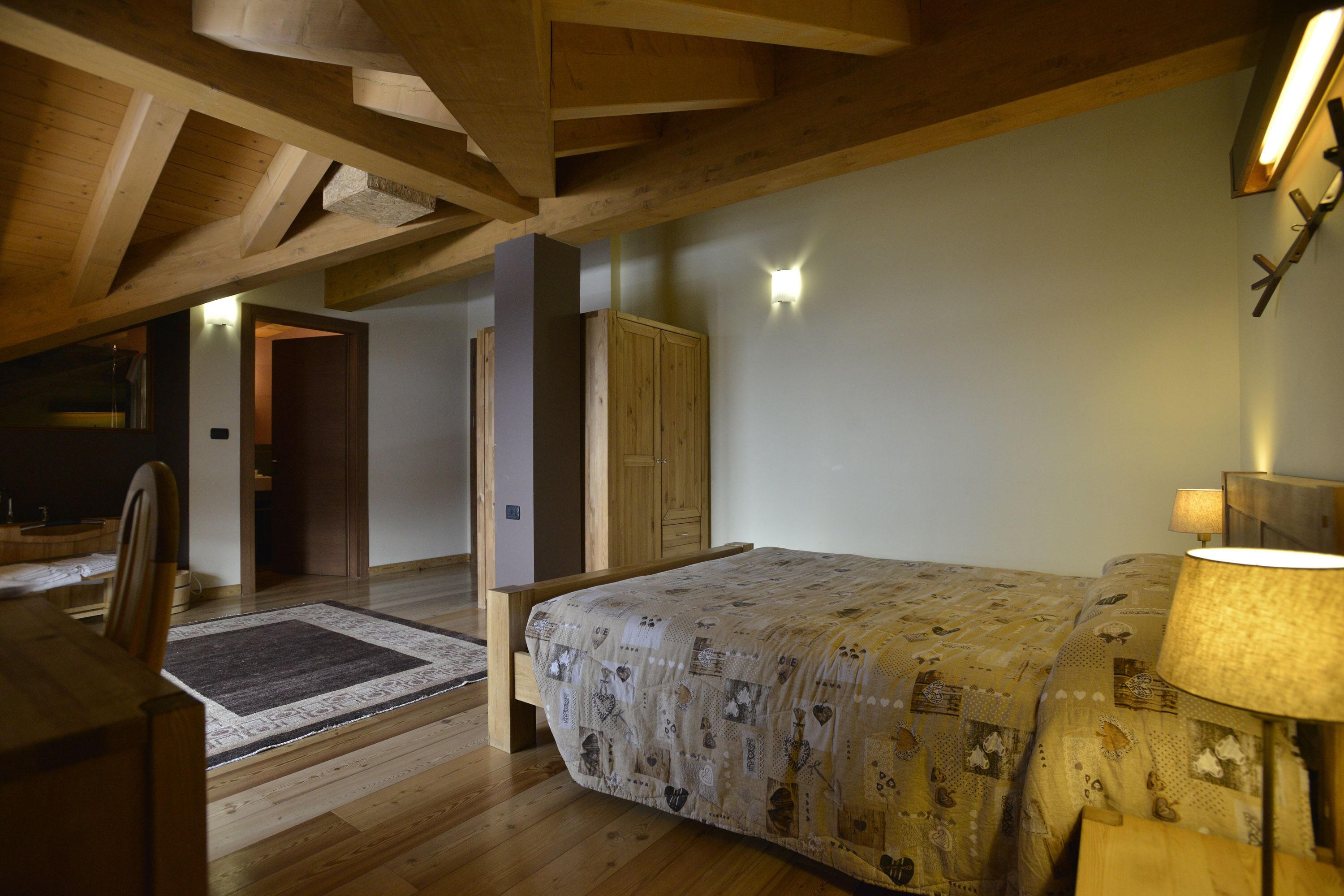 A bedroom with a wooden ceiling, a bed with patterned bedding, a bedside table, and a lamp.