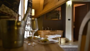 A wooden interior with a wooden table, a glass bottle, and a wine glass. There is a wooden cabinet with a sink and a towel rack. - Hotel La Chance (Gressan)