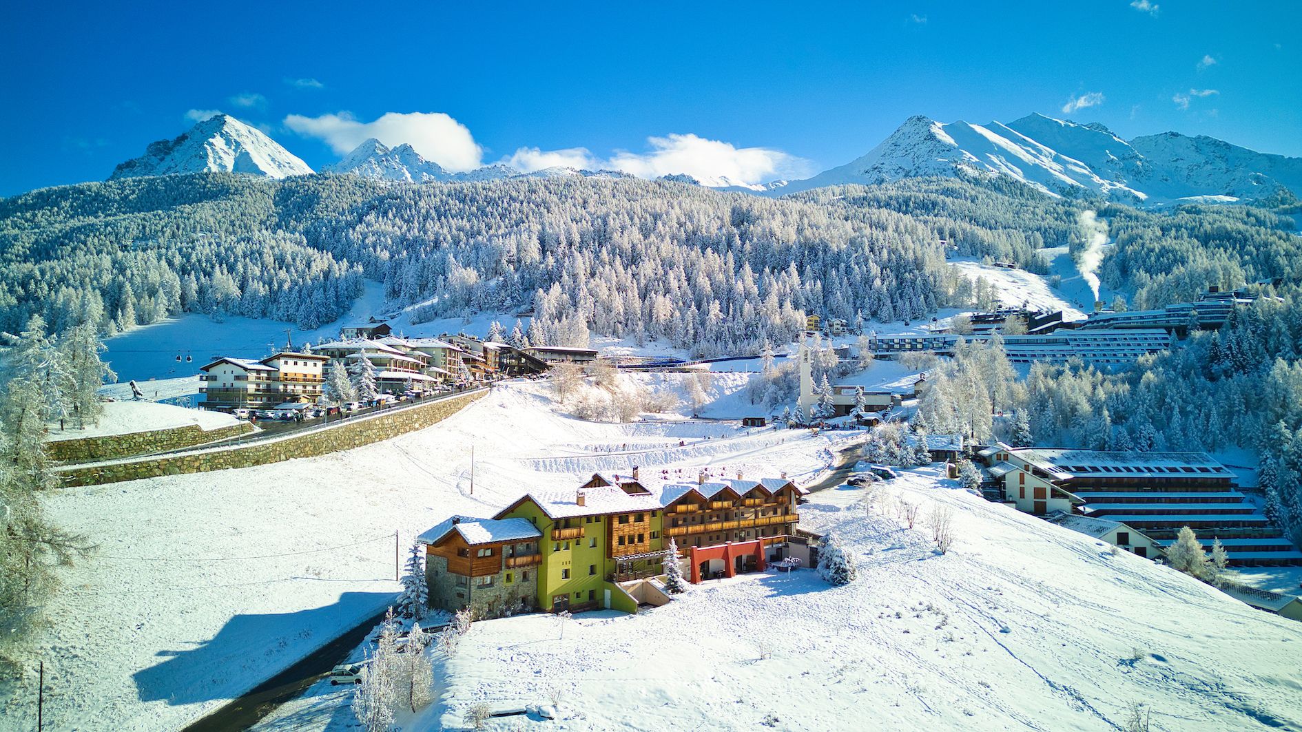 A snow-covered mountain town with buildings, a ski slope, and a lake.