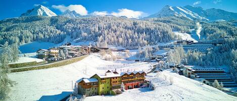 A snow-covered mountain town with buildings, a ski slope, and a lake.