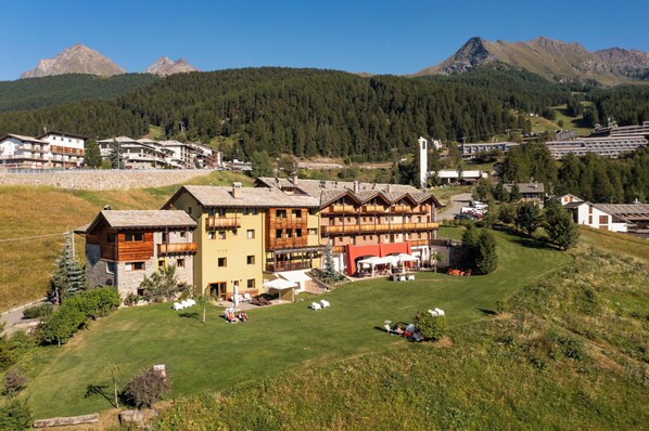 A hotel with multiple buildings, a grassy area, and mountains in the background. - Hotel La Chance (Gressan)