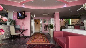A pink-themed lobby with a reception desk, seating area, and a staircase leading to other floors. - La Grotta Hotel (Verona)