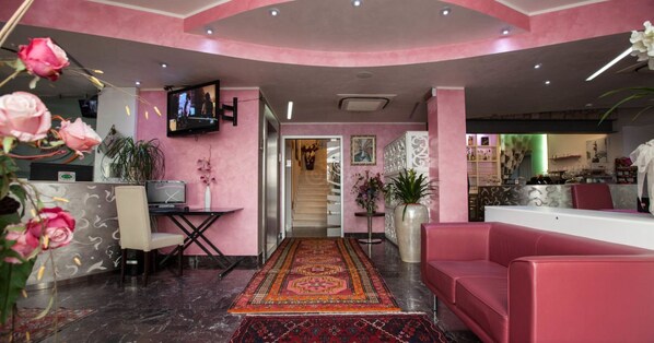 A pink-themed lobby with a reception desk, seating area, and a staircase leading to other floors.