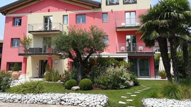 A multi-story building with balconies, a garden with rocks and plants, and a palm tree. - La Grotta Hotel (Verona)