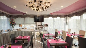 A restaurant with pink tablecloths, black chairs, a chandelier, and a buffet area. - La Grotta Hotel (Verona)