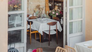 Un espace repas ouvert, agrémenté d’un mur en pierre rustique, de chaises en bois, d’une table dressée avec des nappes blanches et d’une variété de fleurs.