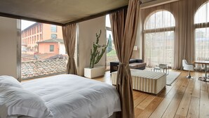 Une chambre d’hôtel dotée d’un grand lit, d’un coin salon avec une table basse et offrant une vue sur le paysage urbain grâce à de grandes fenêtres.