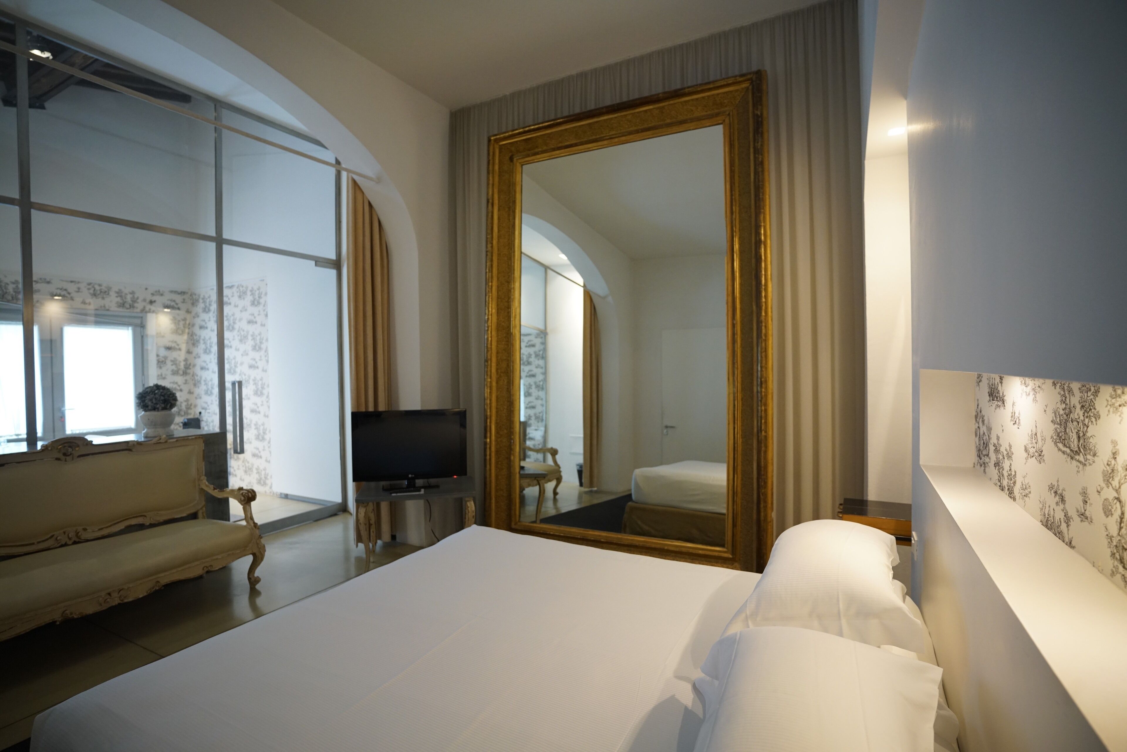 A hotel room with a large bed, a television, a sofa, and a mirror.