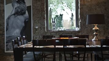 A dining area with a stone wall, a large framed artwork, a table set for four, and a window with a view of greenery.