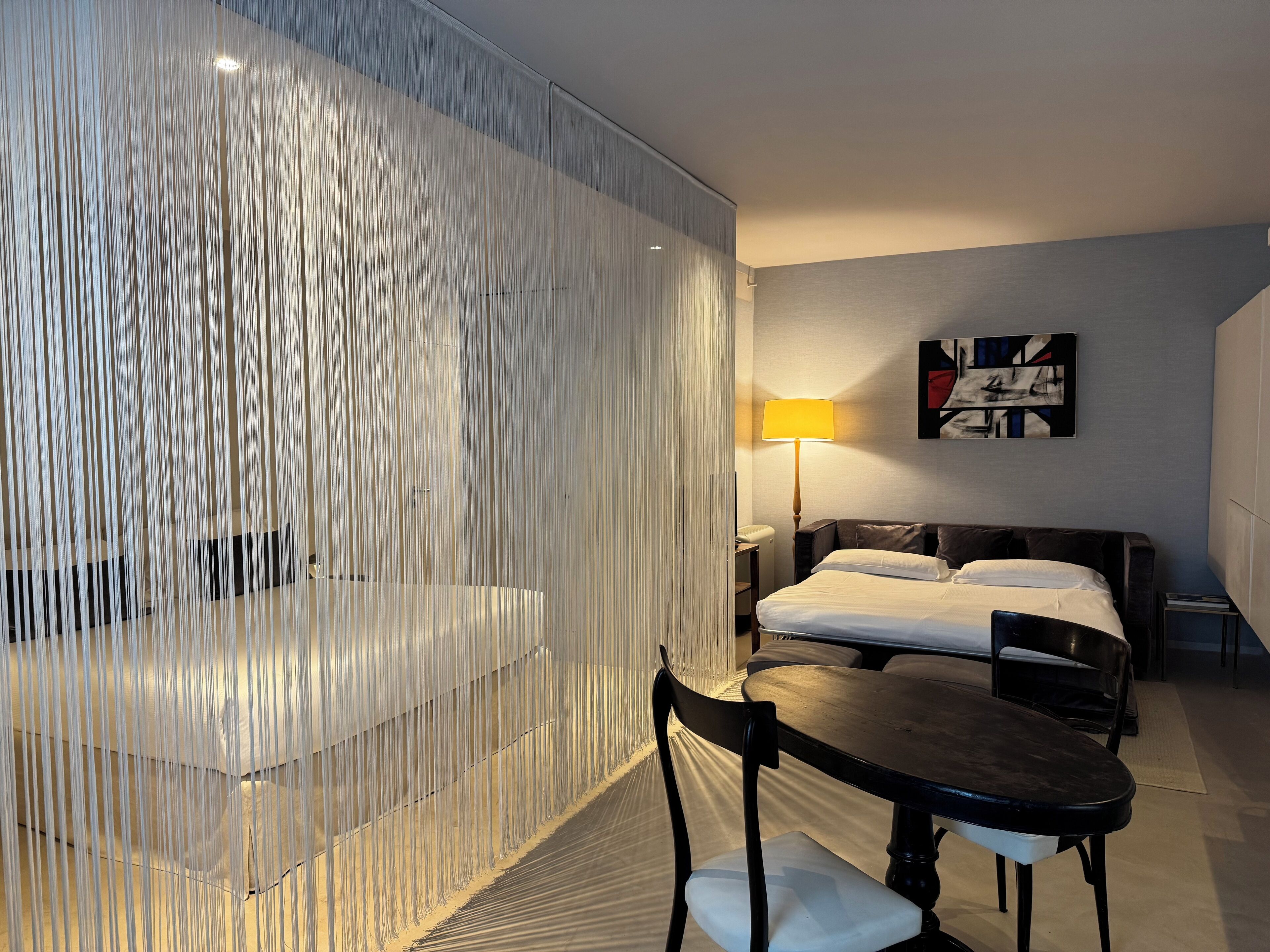 Habitación de hotel con cama, escritorio, silla, lámpara y un cuadro en la pared.