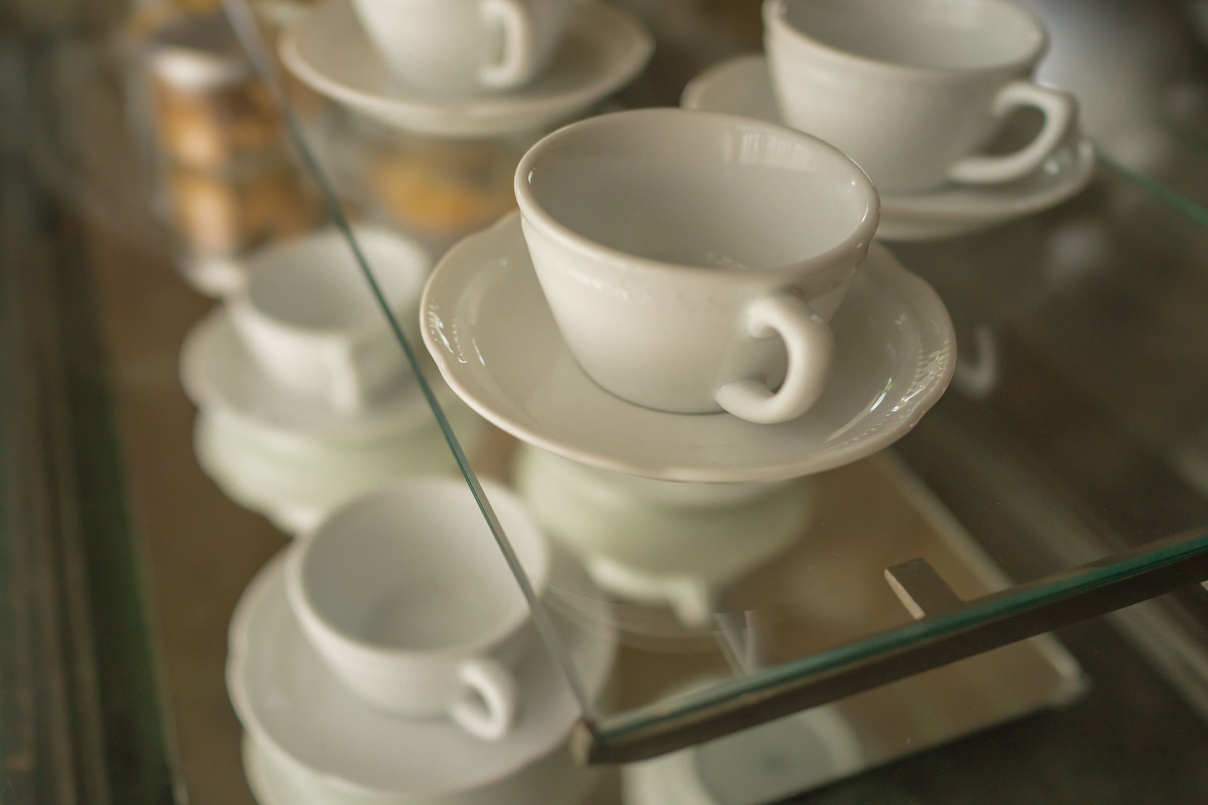 Una presentación de tazas y platones blancos sobre una repisa de vidrio.