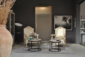 A room with two ornate chairs, a round table, a large vase, and a framed picture on the wall.