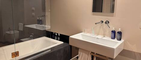 Un baño moderno con una bañera grande, un lavabo y un espejo. Hay artículos de aseo en la encimera del lavabo.