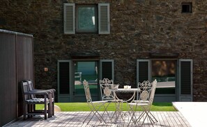 An outdoor patio with a table and chairs, a bench, and a stone building with shutters in the background.