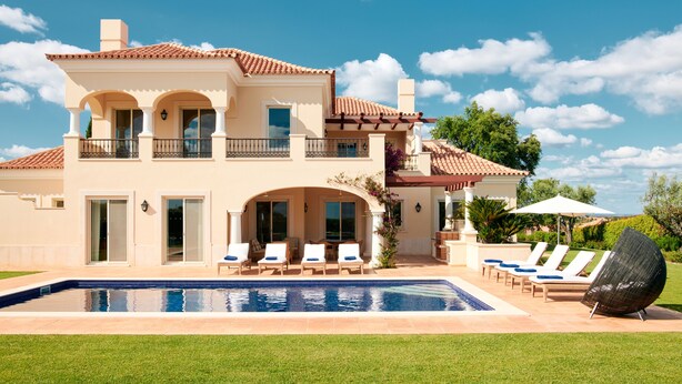 Una casa de dos pisos con piscina, mobiliario exterior y un gran paraguas.