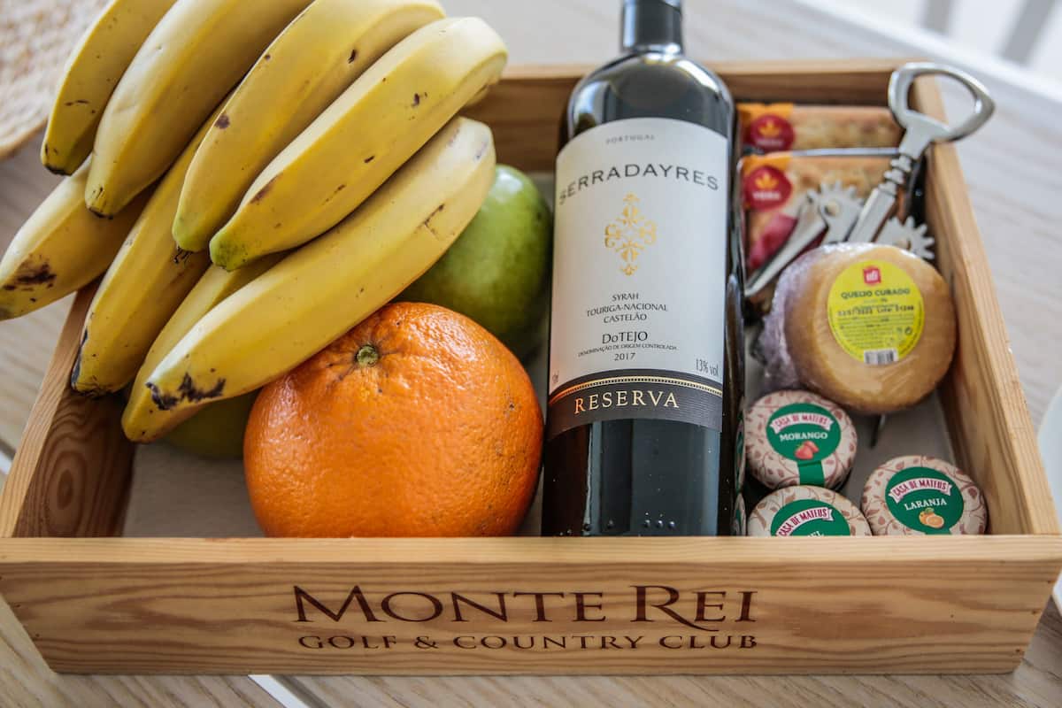 Una caja de madera con una botella de vino, plátanos, una naranja y queso.