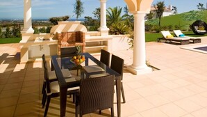 Un patio exterior con una parrilla de ladrillo, una mesa de comedor y sillas, con vistas a un paisaje pintoresco.