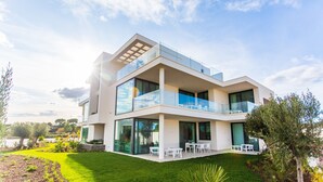 Una casa moderna de dos pisos con techo plano, amplios ventanales y un balcón con mobiliario exterior.