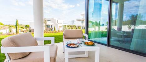 A modern outdoor seating area with a white table and two beige chairs, overlooking a landscaped garden and a residential area.
