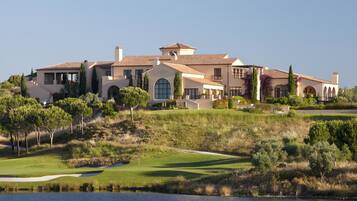 A large, multi-story house with a landscaped lawn and a body of water in the foreground.