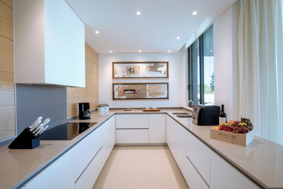 Una cocina moderna con horno empotrado, cafetera y frutero sobre la encimera.