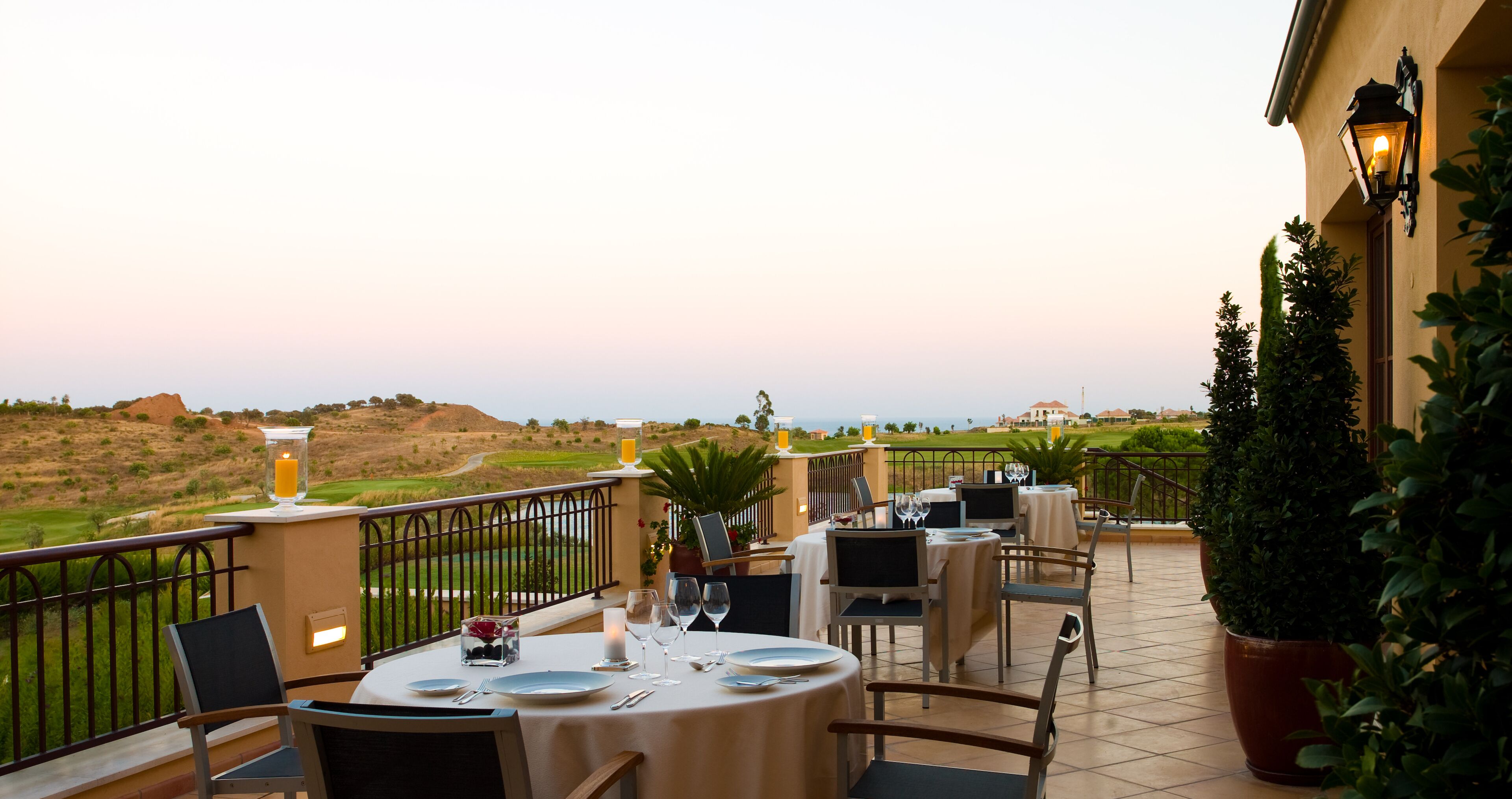 A terrace with tables set for dining, overlooking a golf course and distant landscape.