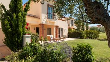 Una casa de dos pisos con un balcón, un patio con mobiliario exterior y un jardín bien cuidado.