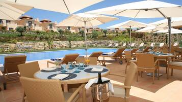 A poolside area with lounge chairs and umbrellas, a pool, and a view of buildings in the background.
